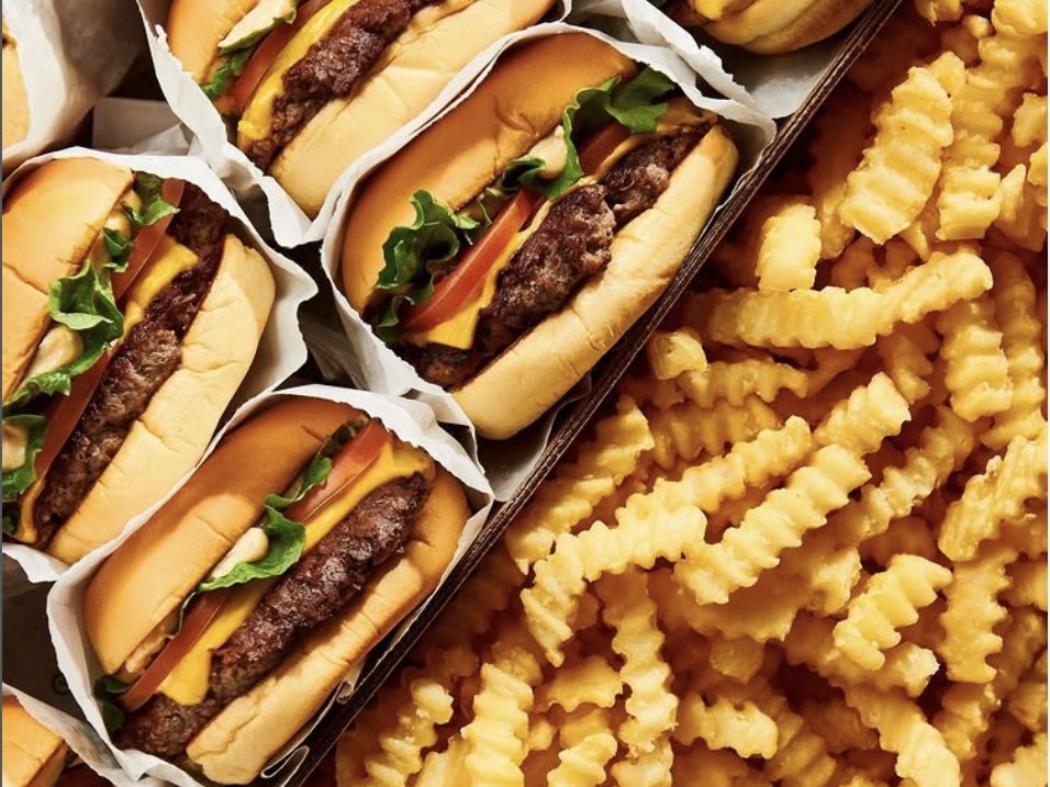 Cheeseburgers in paper wraps beside a tray of crinkle-cut fries